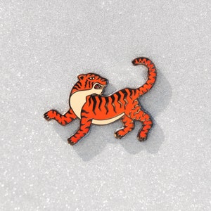 Op de afbeelding: Oranje en zwarte emaille pin van een tijger met een witte buik. De tijger bevindt zich in een rennende houding met zijn staart omhoog gekruld.