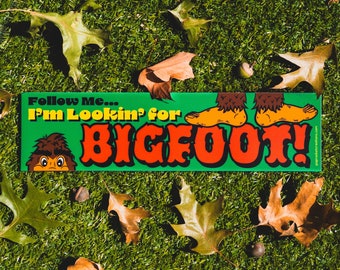Puede incluir: Pegatina para parachoques verde y roja con el texto "Follow Me... I'm Lookin' for BIGFOOT!" y un dibujo animado de Bigfoot con pelaje marrón y fondo verde.