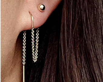 May include: Gold chain earrings with a small gold ball stud on one ear. The chain earrings are dangling and have a straight gold bar at the end.