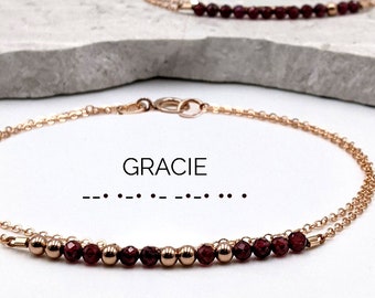 May include: Two delicate gold chain bracelets with red gemstone beads. The top bracelet says "MOMMY" and the bottom bracelet says "GRACIE" with braille dots below.