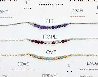 May include: A collection of delicate necklaces with beaded designs. Each necklace features a different color of beads and a word or phrase in Morse code, including "PEACE", "SISTER", "ALWAYS", "BFF", "HOPE", and "LOVE".