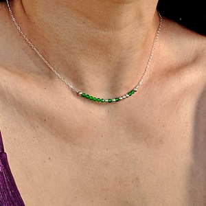 Puede incluir: Un collar de cadena de plata con una fila de pequeñas cuentas de vidrio verde.