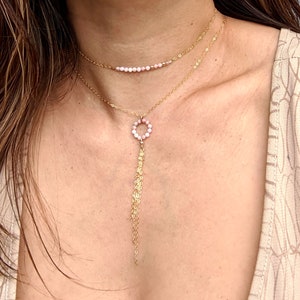 May include: A gold necklace with a pink beaded choker and a long pendant with a circle of pink beads. The necklace is worn by a person with long brown hair. The text "Sister" is written below the image.