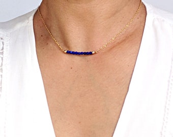 May include: A gold chain necklace with a row of small, dark blue beads.