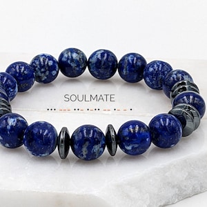 Könnte beinhalten: Ein blaues und schwarzes Perlenarmband mit dem Wort "SOULMATE" auf der weißen Oberfläche, auf der es liegt.