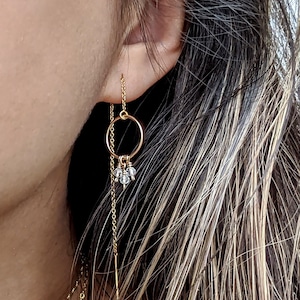 Könnte beinhalten: Goldfarbene Ohrringe mit einem kreisförmigen Design, einer herabhängenden Kette und kleinen, klaren Kristallakzenten. Die Nahaufnahme zeigt die filigrane Kette und wie die Ohrringe am Ohr hängen.