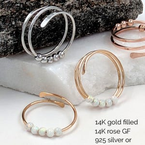 Könnte beinhalten: Eine Auswahl an Ringen in Silber, Gold und Roségold. Einige Ringe haben kleine, runde Perlen, während andere ein Spiraldesign aufweisen. Der Text im Bild lautet: 14K gold filled, 14K rose GF, 925 silver or stainless steel.