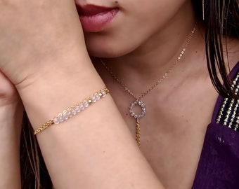 May include: A gold chain necklace with a circle pendant and a gold chain bracelet with clear beads. The necklace and bracelet are worn by a person with long dark hair.