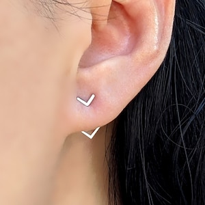 May include: A pair of silver chevron earrings. The earrings are small and delicate, and they are worn in the wearer's earlobes.