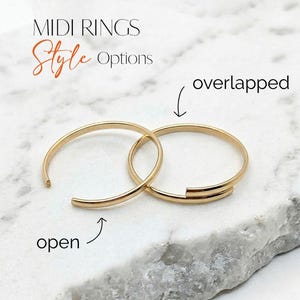 May include: Two gold midi rings are shown on a marble surface. One ring is open, the other is overlapped. The image includes the text "MIDI RINGS Style Options".
