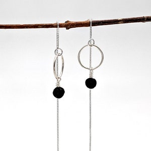 May include: A pair of silver dangle earrings with black lava rock beads and a circle design.