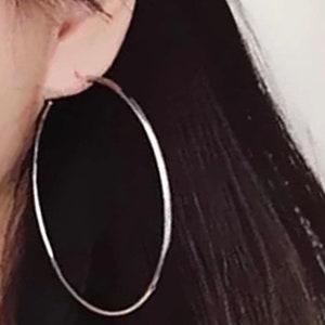Peut inclure: Boucles d'oreilles créoles en argent. Les boucles d'oreilles sont grandes et circulaires, avec une finition lisse et polie.