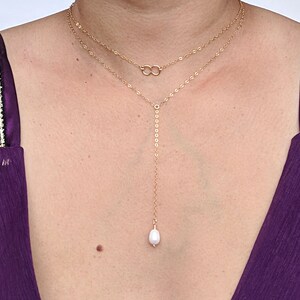 May include: A gold chain necklace with two strands and a single pearl pendant. The necklace is layered and features a delicate chain with a small circle design.