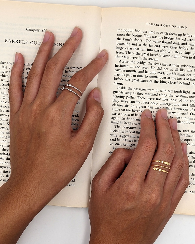 Model hands wearing spiral fidget rings with beads and hammered ends; in sterling silver and gold filled