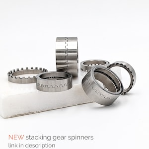 May include: A set of five silver metal gear spinners. The spinners are stacked on top of each other and are arranged in a circle. The spinners are made of metal and have a smooth, polished finish.