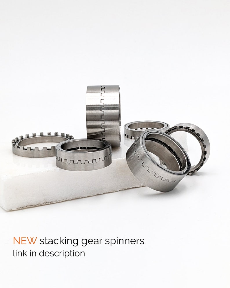 May include: A set of five silver metal gear spinners. The spinners are stacked on top of each other and are arranged in a circle. The spinners are made of metal and have a smooth, polished finish.