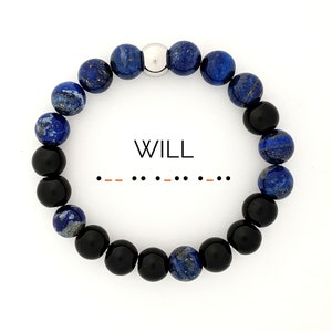 May include: A beaded bracelet with blue and black beads and a silver bead in the centre. The bracelet has the word "WILL" and morse code for the word "WILL" written below it.