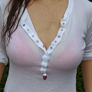 May include: A silver chain necklace with a dark pink, faceted, crystal pendant.