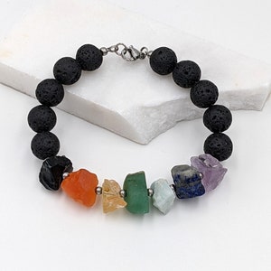 May include: A beaded bracelet featuring black lava rock beads and a series of colorful, raw gemstone chips. The gemstones include black obsidian, carnelian, citrine, green aventurine, aquamarine, lapis lazuli, and amethyst. The bracelet is secured with a silver clasp.