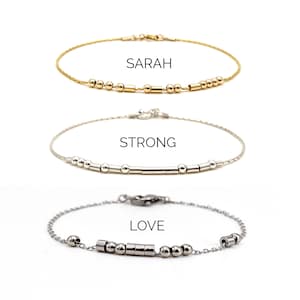 May include: Three delicate bracelets with Morse code designs. The top bracelet is gold-filled and spells "SARAH". The middle bracelet is sterling silver and spells "STRONG". The bottom bracelet is stainless steel and spells "LOVE".