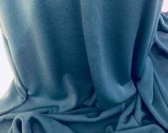 May include: A close-up of a teal blue fabric with a textured surface. The fabric is folded and draped, showing its soft and drapey texture.