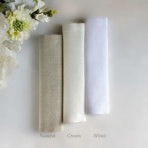 Puede incluir: Tres servilletas de tela rectangulares dobladas verticalmente, dispuestas en fila. Los colores de izquierda a derecha son beige natural, crema y blanco. Cada servilleta tiene una textura tejida visible. Las etiquetas Natural, Cream, White est&aacute;n impresas debajo.