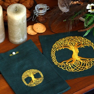 May include: Two green linen placemats with gold embroidered Celtic tree of life designs. The placemats are on a wooden table with candles and cookies.