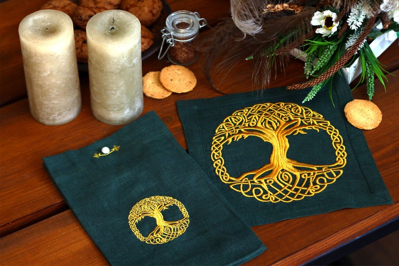 May include: Two green linen placemats with gold embroidered Celtic tree of life designs. The placemats are on a wooden table with candles and cookies.