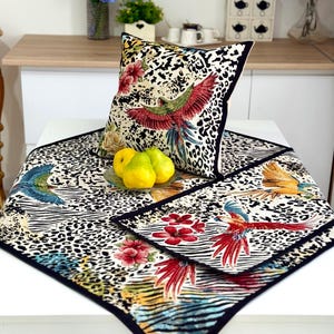 May include: A decorative pillow and table runner set featuring a vibrant parrot design with red, green, and blue feathers, set against a leopard and zebra print background. The set includes a square pillow and a table runner with a black border.
