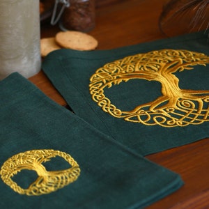 May include: Two green linen coasters with gold embroidered Celtic tree of life designs. The coasters are on a wooden table.