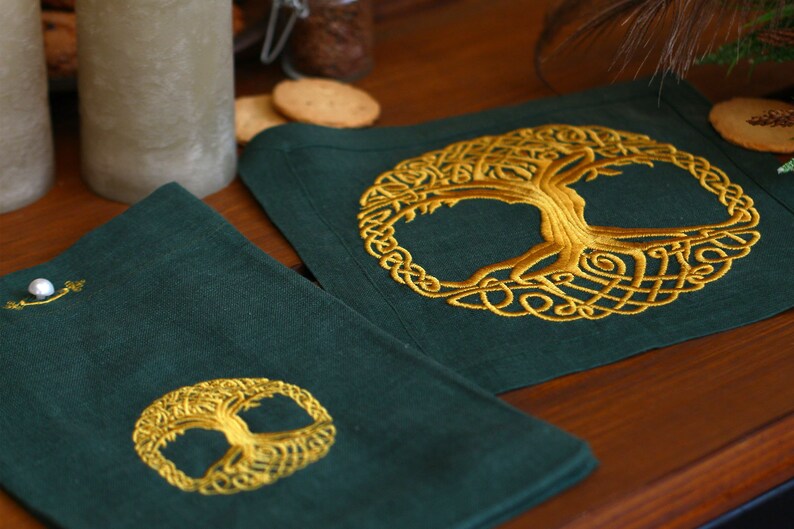May include: Two green linen coasters with gold embroidered Celtic tree of life designs. The coasters are on a wooden table.