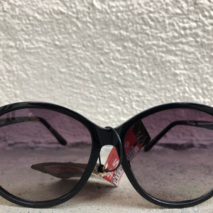 May include: Black cat-eye sunglasses with gold accents. The sunglasses have dark lenses and a reflective surface.