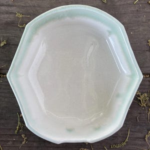 May include: A light green ceramic serving dish with a scalloped edge. The dish is empty and has a white interior.