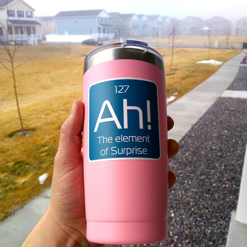 May include: A pink stainless steel travel mug with a white sticker that says "127 Ah! The element of Surprise".