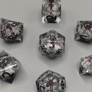 May include: A set of seven clear polyhedral dice, each containing a miniature white sphere with a black spider web pattern and a small red and black spider inside. The dice feature black numbers printed on the exterior surfaces for gameplay.