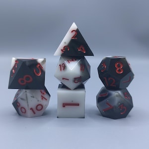 May include: A set of multi-sided dice for tabletop games. The dice are in various shapes, including a pyramid and cube. They are black and white with red numbering, ideal for role-playing games.