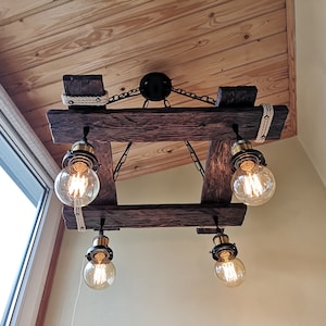 May include: A rustic wooden chandelier with four Edison bulb lights. The chandelier is made of reclaimed wood and has a rope detail. The lights are hanging from chains.