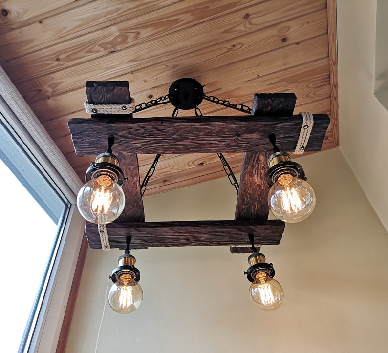 May include: A rustic wooden chandelier with four Edison bulb lights. The chandelier is made of reclaimed wood and has a rope detail. The lights are hanging from chains.