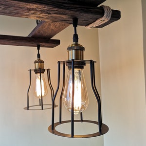 May include: Two black caged pendant lights with gold accents hang from a rustic wooden beam. The lights are turned on and illuminate the room with a warm glow.