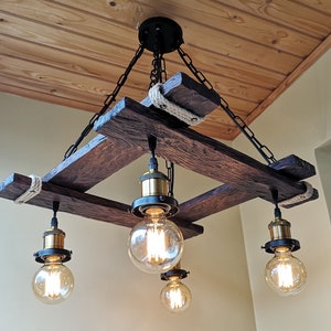 May include: A rustic wooden chandelier with four light bulbs. The chandelier is made of reclaimed wood and has a rope detail. The light bulbs are Edison bulbs and give off a warm glow.