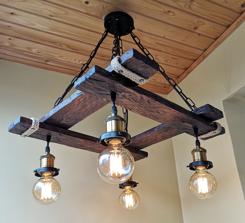 May include: A rustic wooden chandelier with four light bulbs. The chandelier is made of reclaimed wood and has a rope detail. The light bulbs are Edison bulbs and give off a warm glow.