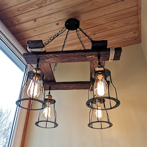 May include: A rustic wooden chandelier with four caged light bulbs. The chandelier is suspended from the ceiling by chains and has a weathered wood finish.