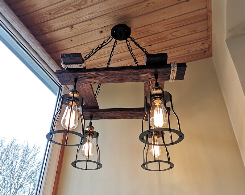 May include: A rustic wooden chandelier with four caged light bulbs. The chandelier is suspended from the ceiling by chains and has a weathered wood finish.