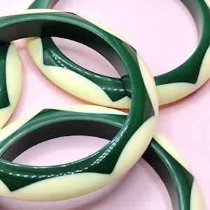 May include: A collection of three circular bangle bracelets featuring a repeating geometric pattern of alternating dark forest green and cream-colored segments. Each bangle has a smooth, polished finish with a consistent, rounded profile.