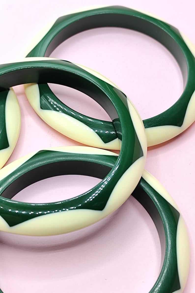 May include: A collection of three circular bangle bracelets featuring a repeating geometric pattern of alternating dark forest green and cream-colored segments. Each bangle has a smooth, polished finish with a consistent, rounded profile.