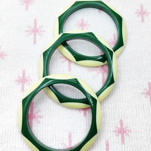 May include: Three circular bangles featuring a geometric design with alternating segments of dark forest green and cream-colored material. Each bangle has a smooth, polished finish with a repeating star-like pattern created by the green sections.