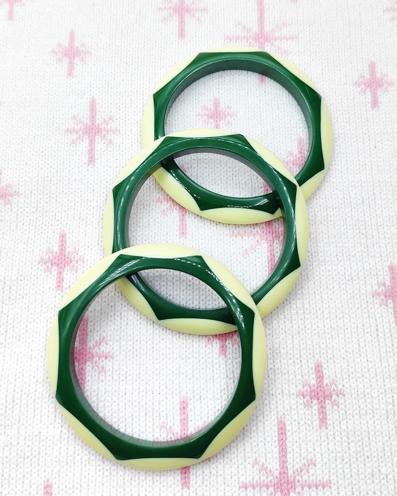 May include: Three circular bangles featuring a geometric design with alternating segments of dark forest green and cream-colored material. Each bangle has a smooth, polished finish with a repeating star-like pattern created by the green sections.