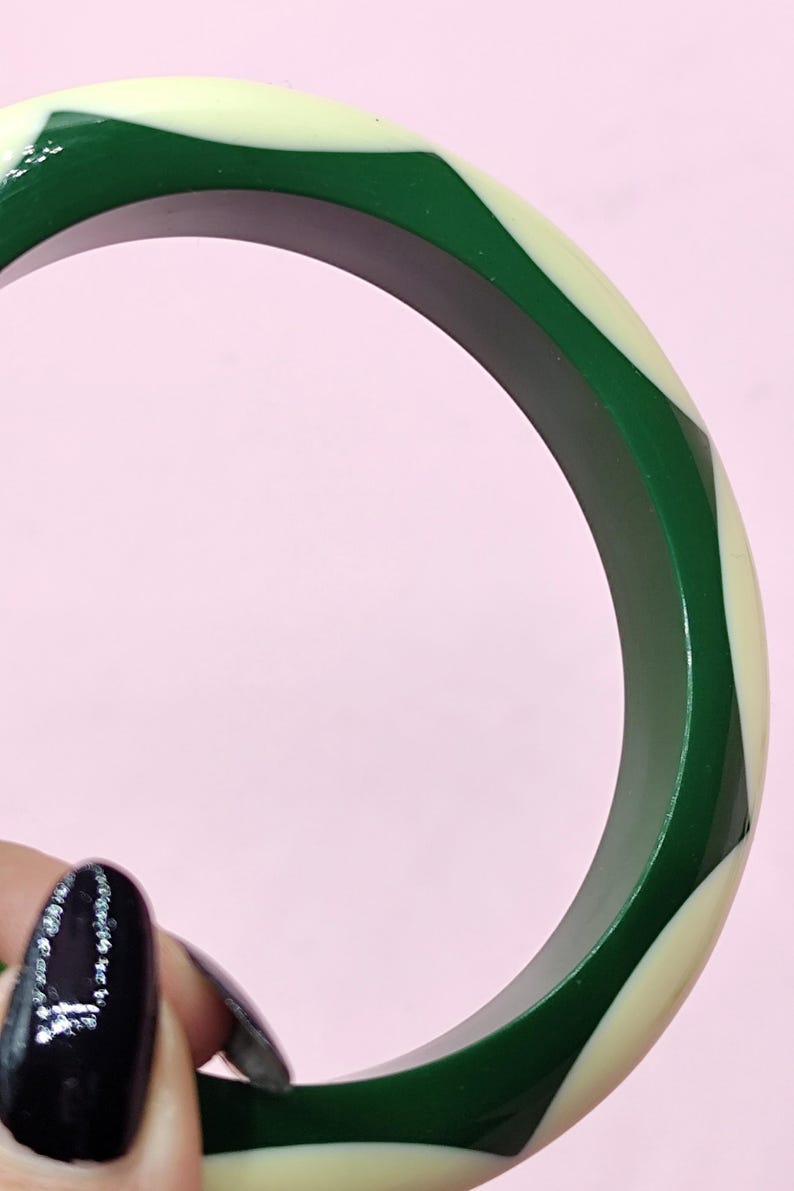 May include: A circular bangle bracelet featuring a repeating geometric pattern of alternating dark forest green and cream-colored segments. The bangle has a smooth, polished finish and a thick, rounded profile that creates a bold, high-contrast look.
