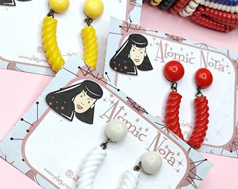 May include: Three pairs of vintage style earrings with a retro design. The earrings are made of plastic and feature a twisted, spiral shape. The earrings are available in yellow, red, and white.