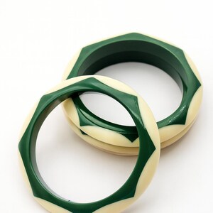 May include: Two circular bangles featuring a smooth, glossy finish. Each bangle displays an alternating geometric pattern of dark forest green and cream-colored segments, creating a repeating star-like design around the entire circumference.